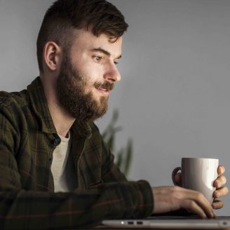 Man with laptop at desk in a dark room with coffee cup